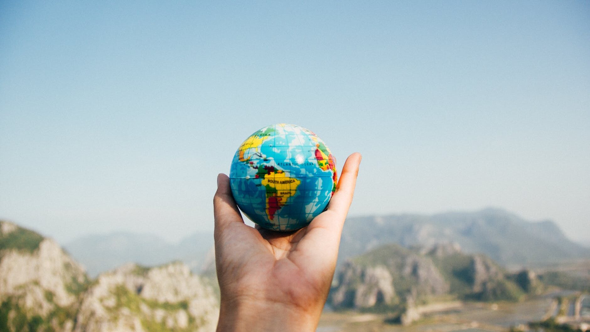 person holding world globe facing mountain